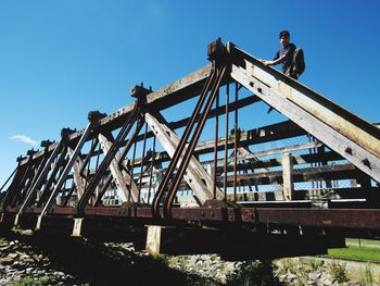 Low angle view of boy on metallic bridge against sky