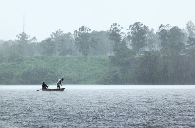 Men sailing on rowboat in river during rain