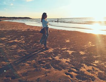 Rear view of woman standing at beach during sunset