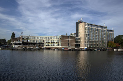 View of buildings by river against cloudy sky