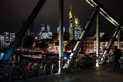 Illuminated bridge by buildings against sky at night