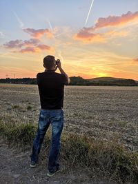 Rear view of man standing on field against sky during sunset