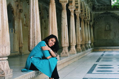 Portrait of smiling young woman sitting at historic building