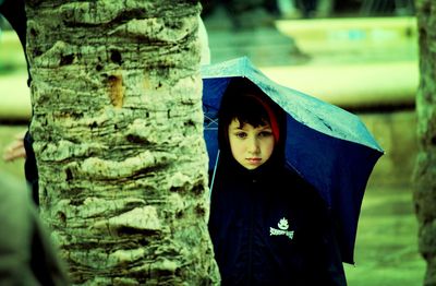 Portrait of young woman standing on tree trunk