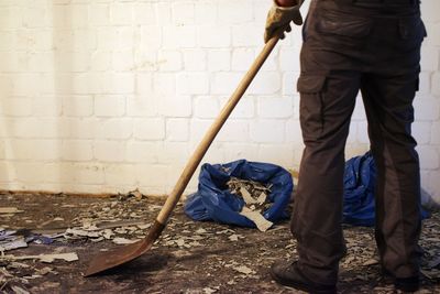 Low section of man with work tool standing against wall