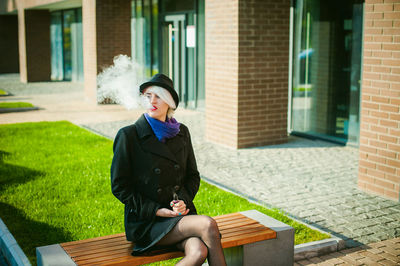 Young woman smoking while sitting on bench at park