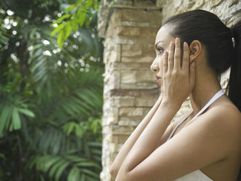 Side view of woman holding face outdoors