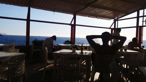 People at restaurant by sea against sky seen through window