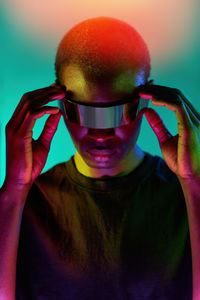Focused cool young african american in black t shirt adjusting modern futuristic goggles while experiencing virtual reality in studio with colorful neon lights