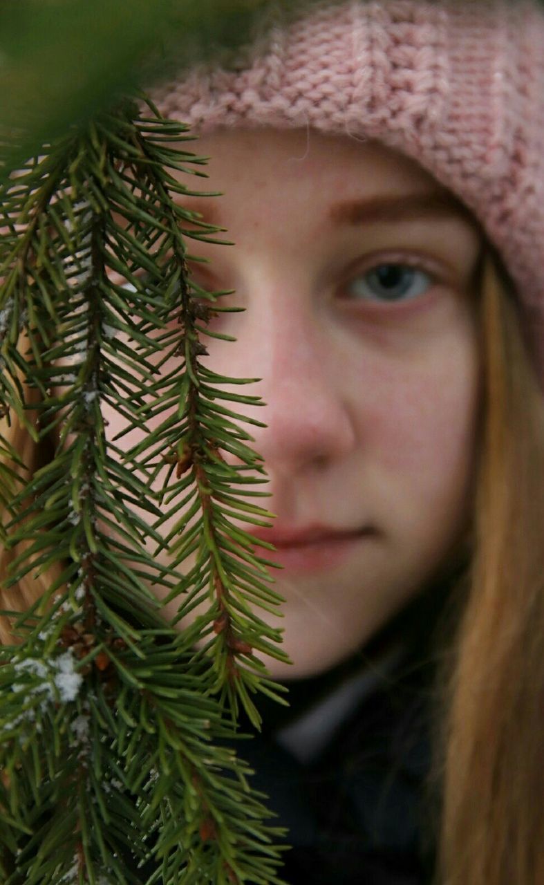 one person, portrait, plant, close-up, real people, headshot, green color, tree, women, lifestyles, hat, clothing, selective focus, winter, nature, human face, young adult, day, christmas, pine tree, warm clothing, needle - plant part, coniferous tree