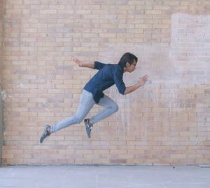 Side view of young man levitating against brick wall