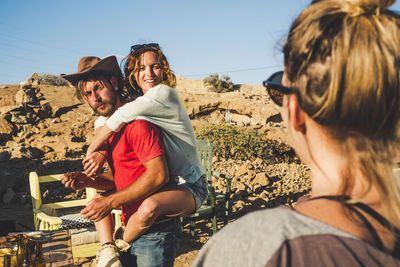 Rear view of woman looking at friends piggybacking against sky