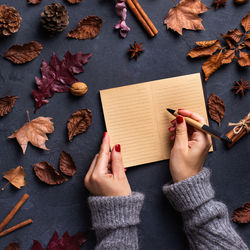 Autumn fall thanksgiving day composition with dried leaves. female hands writing in notebook