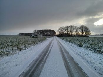 Road passing through field against cloudy sky