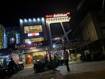 People on street against illuminated buildings in city at night