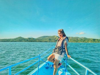 Portrait of smiling young woman in boat sailing on sea against blue sky