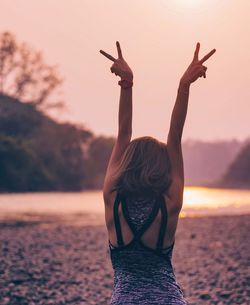 Rear view of woman standing at beach during sunset