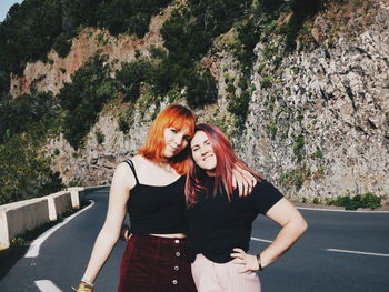 Portrait of friends standing on road against mountain during sunny day