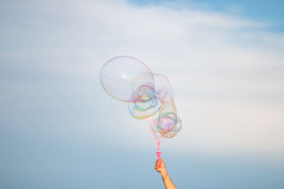 Low angle view of person holding bubbles against sky