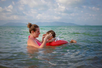 Mother and daughter swimming in sea against sky