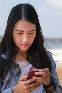 Beautiful woman using mobile phone while standing against sky