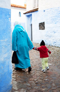 Rear view of woman with child walking at alley amidst houses