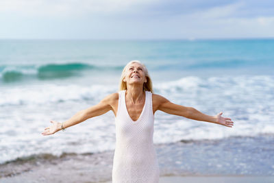 Senior woman with arms raised standing on beach