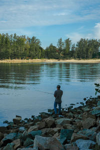 Man standing on rock by lake against sky