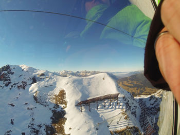 Close-up of in person in overhead cable car on snowcapped mountain against sky