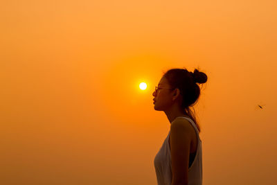 Young woman standing against clear orange sky