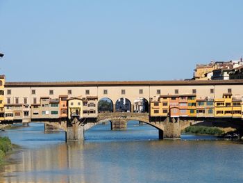 Arch bridge over river in city against clear sky