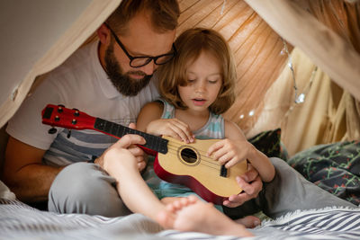 Portrait of a 6 year old boy and his father having fun playing guitar in teepee tent.