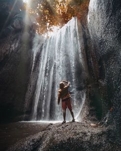 Rear view of man standing on rock against waterfall