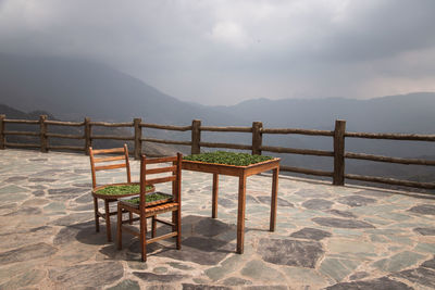 Chairs and table at tea plantation against sky