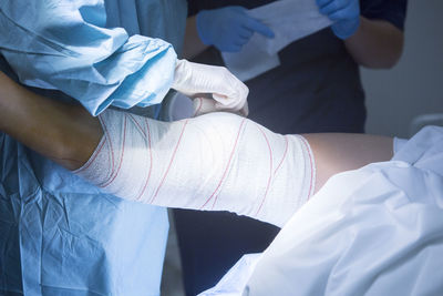 Midsection of doctor applying bandage on patient leg at hospital