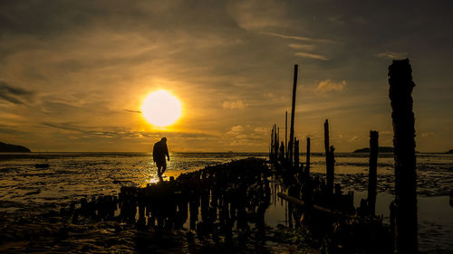 Silhouette people standing on beach against sky during sunset