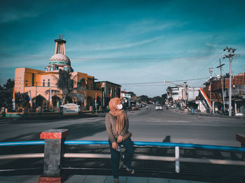 Rear view of woman walking on city street against sky