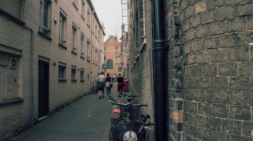 Rear view of people walking amidst buildings on street in city
