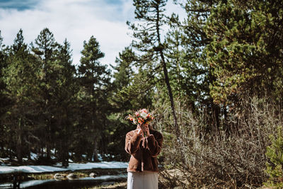 Rear view of woman standing by trees in forest