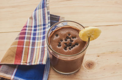 Chocolate banana smoothie topping sprinkled with chocolate chips banana slices on a wooden floor.