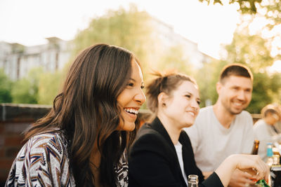 Happy young woman sitting with male and female friends at garden party