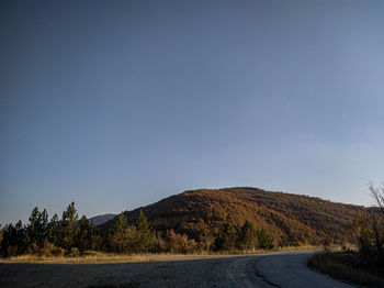 Scenic view of road by mountains against clear blue sky