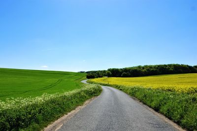 Road amidst field against clear blue sky