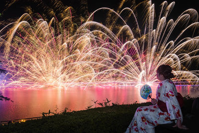 Rear view of woman with firework display at night