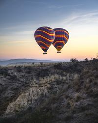 Hot air balloon flying over land against sky during sunset