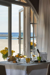 Glass of table by sea against sky seen through window