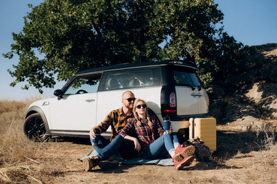 Young men sitting on car against trees