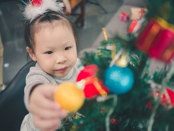 Close-up of cute baby girl touching bauble hanging from christmas tree at home