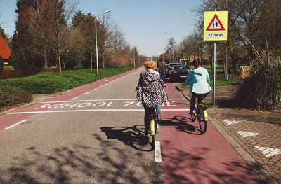 Rear view of women riding bicycle on road against sky