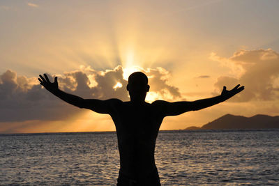 Silhouette of man with the arms a cross on beach at sunset